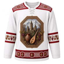 Load image into Gallery viewer, Georgia Original Hockey Jersey in Kazbegi Snow White, front view – ornate knotwork-and-grapevine yoke and a crest of Svaneti stone tower houses with qvevri and panduri, detailed artwork, custom name and number