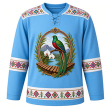Load image into Gallery viewer, Guatemala Original Hockey Jersey in Atitlán Sky Blue, front view – ornate quetzal, Monja Blanca orchid, Lake Atitlán volcanoes and marimba crest, huipil-brocade yoke, detailed illustrated artwork, custom name and number