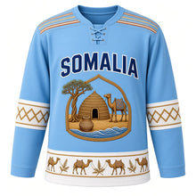Load image into Gallery viewer, Somalia Original Hockey Jersey in Somali Sky Blue, front view – alindi-stripe yoke and aqal-dome crest with camel, frankincense tree and dhiil vessel, ornate detailed artwork, custom name and number