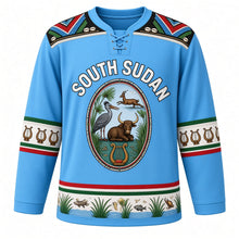 Load image into Gallery viewer, South Sudan Original Hockey Jersey in White Nile Blue, front view – ornate beaded oval crest with long-horned bull, shoebill and kob, Dinka beadwork yoke, detailed artwork, custom name and number