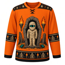 Load image into Gallery viewer, Ugly Halloween Mummy Tomb Crawl Hockey Jersey in Pumpkin Orange, front view – pumpkin orange body with black yoke with a glowing-eyed bandaged mummy rising from an open sarcophagus with tomb torches and scarab beetles, hieroglyph-style yoke, bandage sleeve bands and a scarab hem band – custom name and number