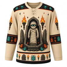 Load image into Gallery viewer, Ugly Halloween Mummy Tomb Crawl Hockey Jersey in Tomb Sand, front view – tomb sand body with black yoke with a glowing-eyed bandaged mummy rising from an open sarcophagus with tomb torches and scarab beetles, hieroglyph-style yoke, bandage sleeve bands and a scarab hem band – custom name and number