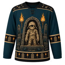 Load image into Gallery viewer, Ugly Halloween Mummy Tomb Crawl Hockey Jersey in Cursed Teal, front view – cursed teal body with black yoke with a glowing-eyed bandaged mummy rising from an open sarcophagus with tomb torches and scarab beetles, hieroglyph-style yoke, bandage sleeve bands and a scarab hem band – custom name and number