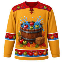 Load image into Gallery viewer, Ugly Thanksgiving Apple Bobbing Barrel Hockey Jersey in Cider Gold, front view – cider gold body with apple red yoke, a wooden barrel tub of water with red and green apples splashing, hay bales, apples and oak leaves around the base, a yoke of apples floating on water ripples and sleeve and hem bands of apples floating on blue water with droplets – custom name and number