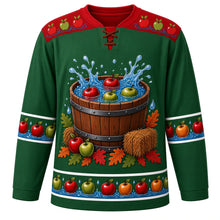 Load image into Gallery viewer, Ugly Thanksgiving Apple Bobbing Barrel Hockey Jersey in Orchard Green, front view – orchard green body with apple red yoke, a wooden barrel tub of water with red and green apples splashing, hay bales, apples and oak leaves around the base, a yoke of apples floating on water ripples and sleeve and hem bands of apples floating on blue water with droplets – custom name and number