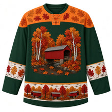 Load image into Gallery viewer, Ugly Thanksgiving Covered Bridge Foliage Hockey Jersey in Hemlock Green, front view – hemlock green body with foliage orange yoke, a red wooden covered bridge with a gray roof over a rocky creek among white birch trunks and round fluffy autumn trees, oak leaves on the water, rounded oak-leaf yoke, birch-bark sleeve bands with oak leaves and a hem band of little red covered bridges among fall trees – custom name and number