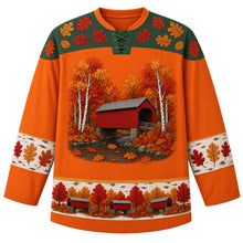 Load image into Gallery viewer, Ugly Thanksgiving Covered Bridge Foliage Hockey Jersey in Foliage Orange, front view – foliage orange body with hemlock green yoke, a red wooden covered bridge with a gray roof over a rocky creek among white birch trunks and round fluffy autumn trees, oak leaves on the water, rounded oak-leaf yoke, birch-bark sleeve bands with oak leaves and a hem band of little red covered bridges among fall trees – custom name and number