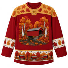 Load image into Gallery viewer, Ugly Thanksgiving Covered Bridge Foliage Hockey Jersey in Bridge Red, front view – barn red body with birch gold yoke, a red wooden covered bridge with a gray roof over a rocky creek among white birch trunks and round fluffy autumn trees, oak leaves on the water, rounded oak-leaf yoke, birch-bark sleeve bands with oak leaves and a hem band of little red covered bridges among fall trees – custom name and number