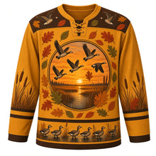 Load image into Gallery viewer, Ugly Thanksgiving Goose Flock Migration Hockey Jersey in Prairie Gold, front view – prairie gold body with marsh brown yoke, a round sunset marsh crest with five flying geese ringed by oak and oval leaves, a yoke with two flying geese and leaves, cattails on the sleeves and a hem band of geese waddling among cattails at the water – custom name and number