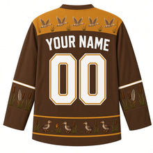 Load image into Gallery viewer, Ugly Thanksgiving Goose Flock Migration Hockey Jersey in Marsh Brown, back view – marsh brown body with prairie gold yoke with a row of five flying geese and little cattails, cattail-and-feather sleeve bands, a hem band of goslings among cattails, straight YOUR NAME lettering and 00 – custom name and number