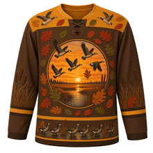 Load image into Gallery viewer, Ugly Thanksgiving Goose Flock Migration Hockey Jersey in Marsh Brown, front view – marsh brown body with prairie gold yoke, a round sunset marsh crest with five flying geese ringed by oak and oval leaves, a yoke with two flying geese and leaves, cattails on the sleeves and a hem band of geese waddling among cattails at the water – custom name and number