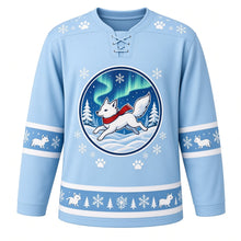 Load image into Gallery viewer, Ugly Christmas Arctic Fox Frolic Hockey Jersey in Glacier Blue, front view – glacier blue body with a round badge of a white arctic fox in a red scarf leaping through snow under green aurora lights with pines, paw-print and snowflake yoke and little-fox sleeve and hem bands – custom name and number