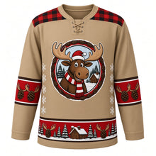 Load image into Gallery viewer, Ugly Christmas Moose Lodge Hockey Jersey in Woodland Tan, front view – woodland tan body with red-and-black plaid yoke with a round cartoon moose crest with a striped scarf by a snowy log cabin, plaid yoke, antler and pinecone sleeve bands and a pinecone hem band – custom name and number
