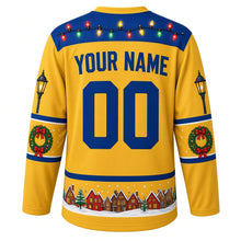 Load image into Gallery viewer, Ugly Christmas Christmas Village Lights Hockey Jersey in Starlight Gold, back view with a string-light yoke, street-lamp and wreath sleeve bands, snowy rooftop hem band, arched YOUR NAME lettering and 00 – custom name and number