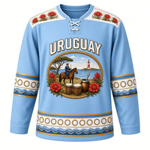 Load image into Gallery viewer, Uruguay Original Hockey Jersey in Celeste Sky, front view – ornate oval cameo crest with gaucho, ombú tree, candombe drums and ceibo flowers, detailed artwork, custom name and number