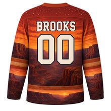 Load image into Gallery viewer, USA Patriotic Canyon Sunset Flag Hockey Jersey in Red Rock Sienna, back view with your name and number – burnt sienna canyon layers beneath an orange sunset sky